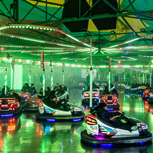 Der Autoscooter ist grün beleuchtet und viele Besucher fahren auf der Fläche mit unterschiedlichen Chaisen