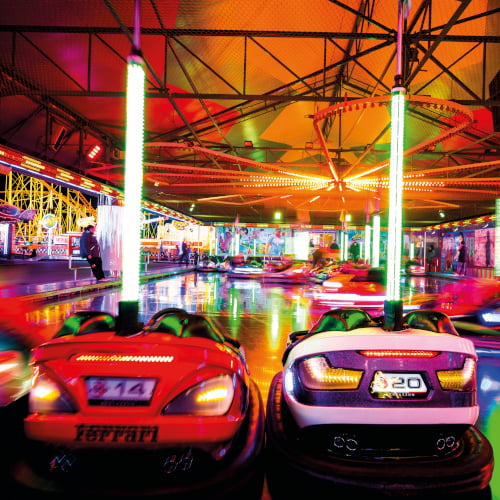 Man sieht eine rote und eine lilane Chaise von hinten. Im Hintergrund ist der restlich Autoscooter bunt beleuchtet