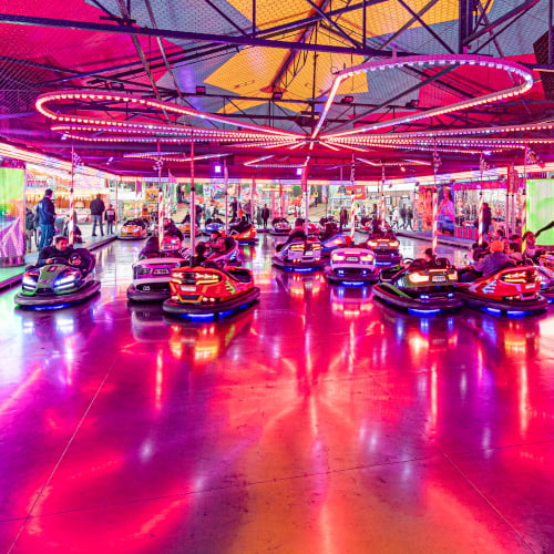 Die Autoscooter-Fläche ist rot und lila beleuchtet und viele Chaisen fahren umher