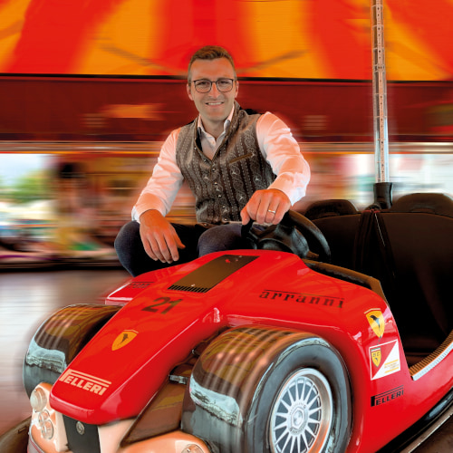 Florian Diebold sitzt lachend in einer roten Chaise und der Hintergrund ist dynamisch verschwommen